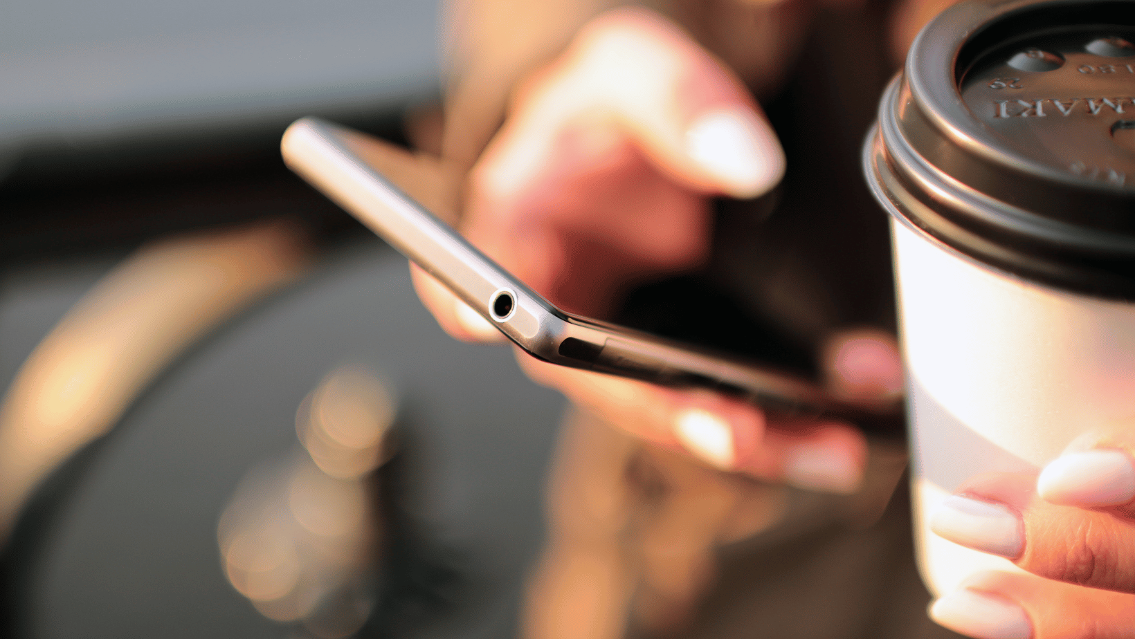 Person on mobile phone with coffee in hand.